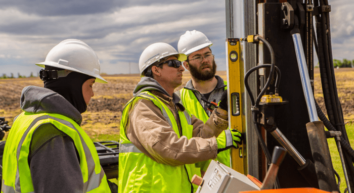 Three solar installers checking the level on a pile driver machine. 